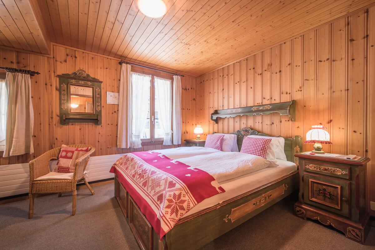 Una habitación con paneles de madera, una cama, una silla, una mesita de noche y un espejo.