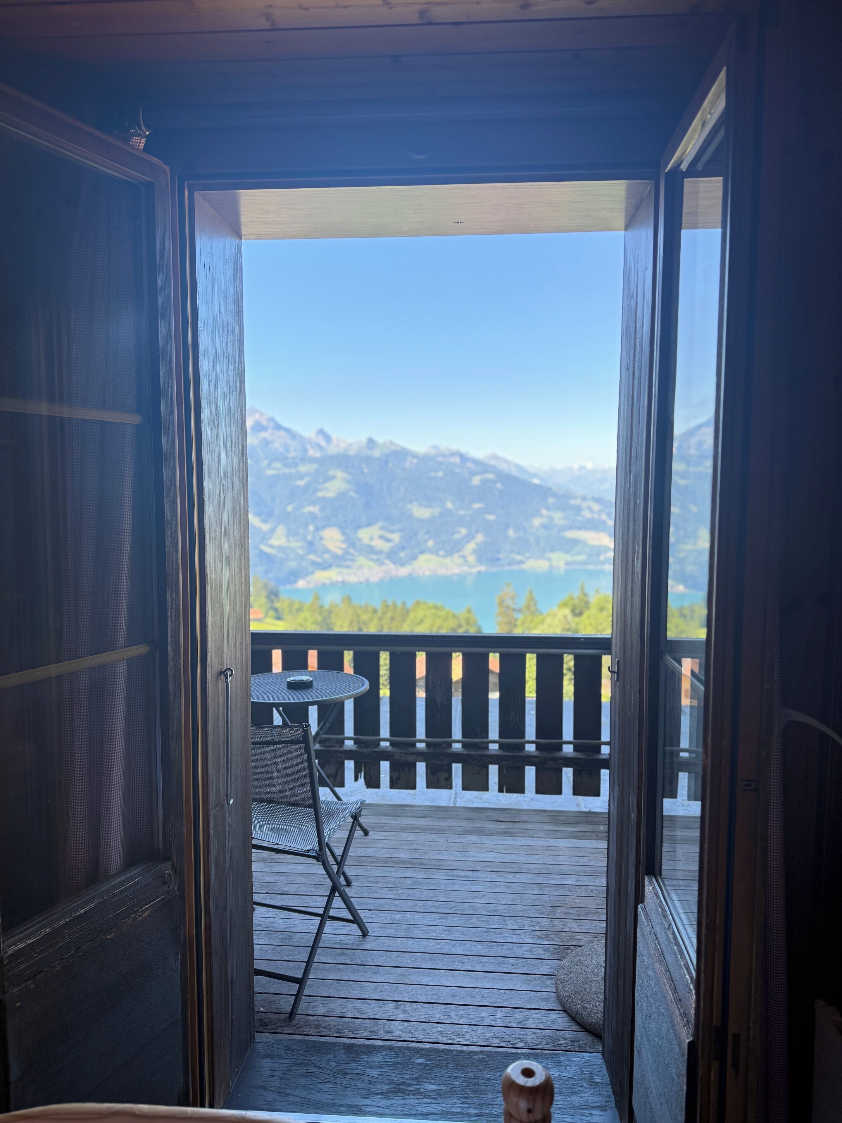Eine offene Tür, die zu einem Balkon mit Blick auf Berge und einen See führt.