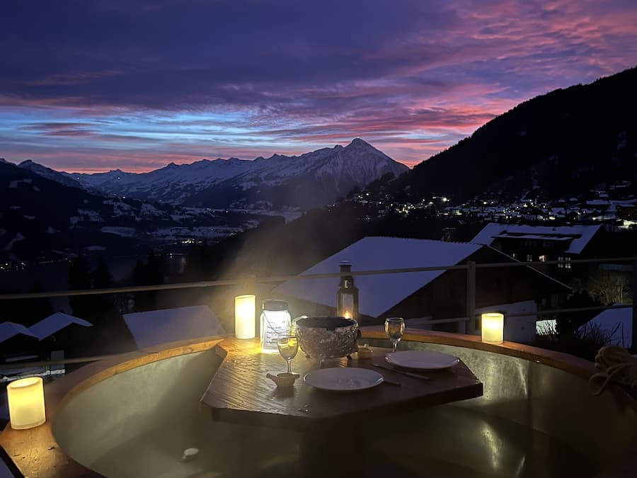 Tinaja de madera con velas y un recipiente de vidrio, rodeada de montañas nevadas y un cielo crepuscular.