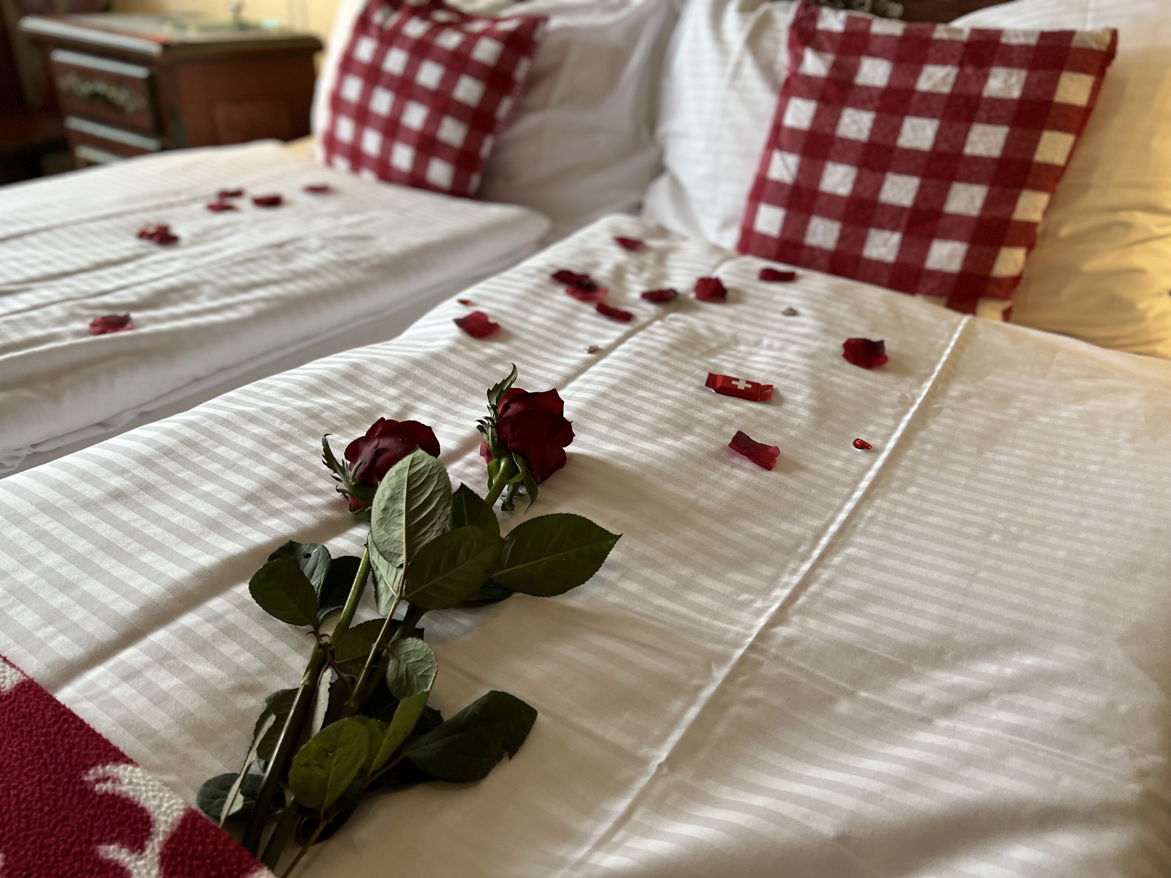 Habitación de hotel con dos camas, cada una con cubrecama blanco y almohadones blancos y rojos a cuadros.