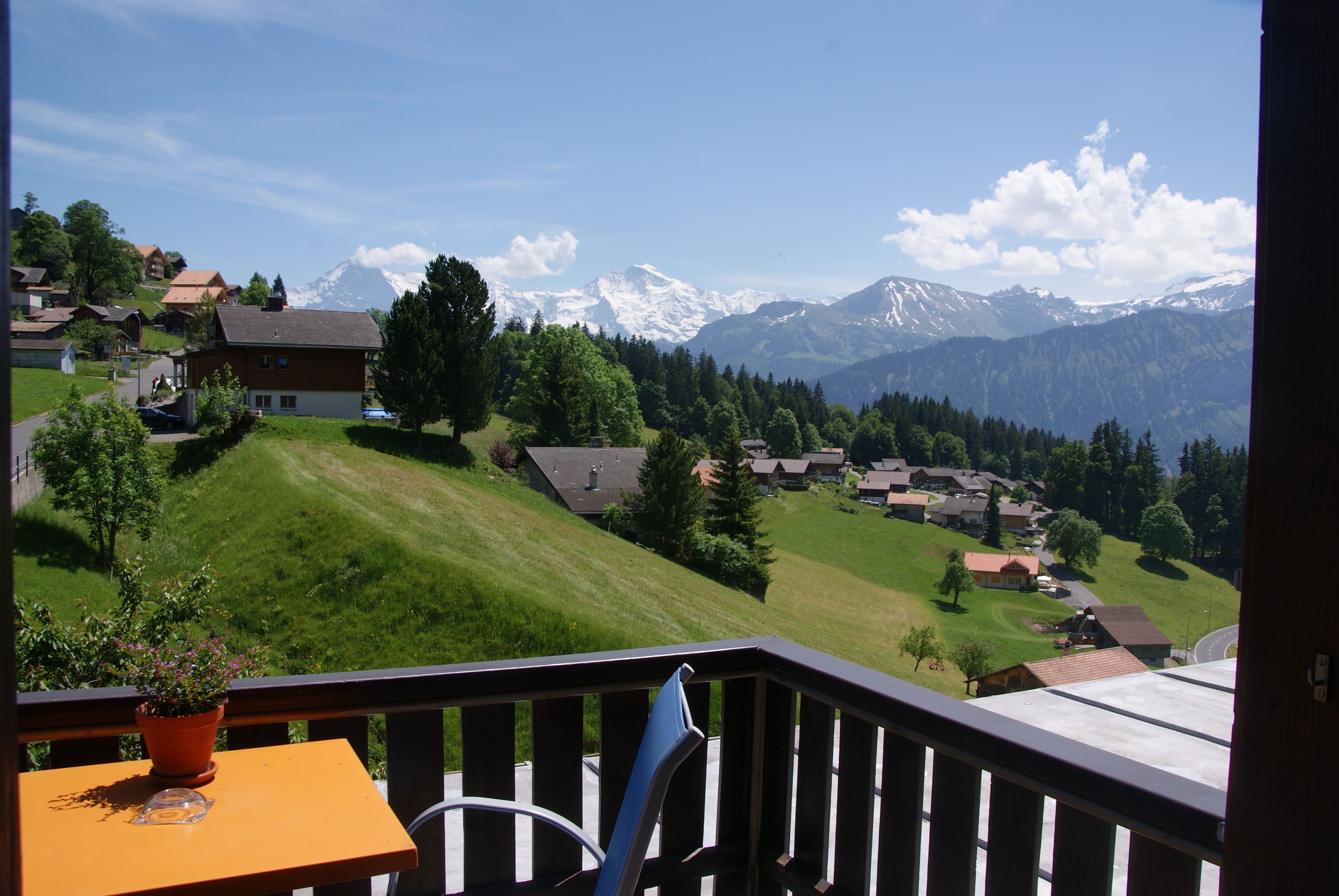 Ein Balkon mit Blick auf ein Gebirge, eine grüne Wiese und eine Reihe von Häusern.