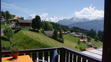 Ein Balkon mit Blick auf ein Gebirge, eine grüne Wiese und eine Reihe von Häusern.