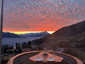 A table set for two with a view of a sunset over mountains.