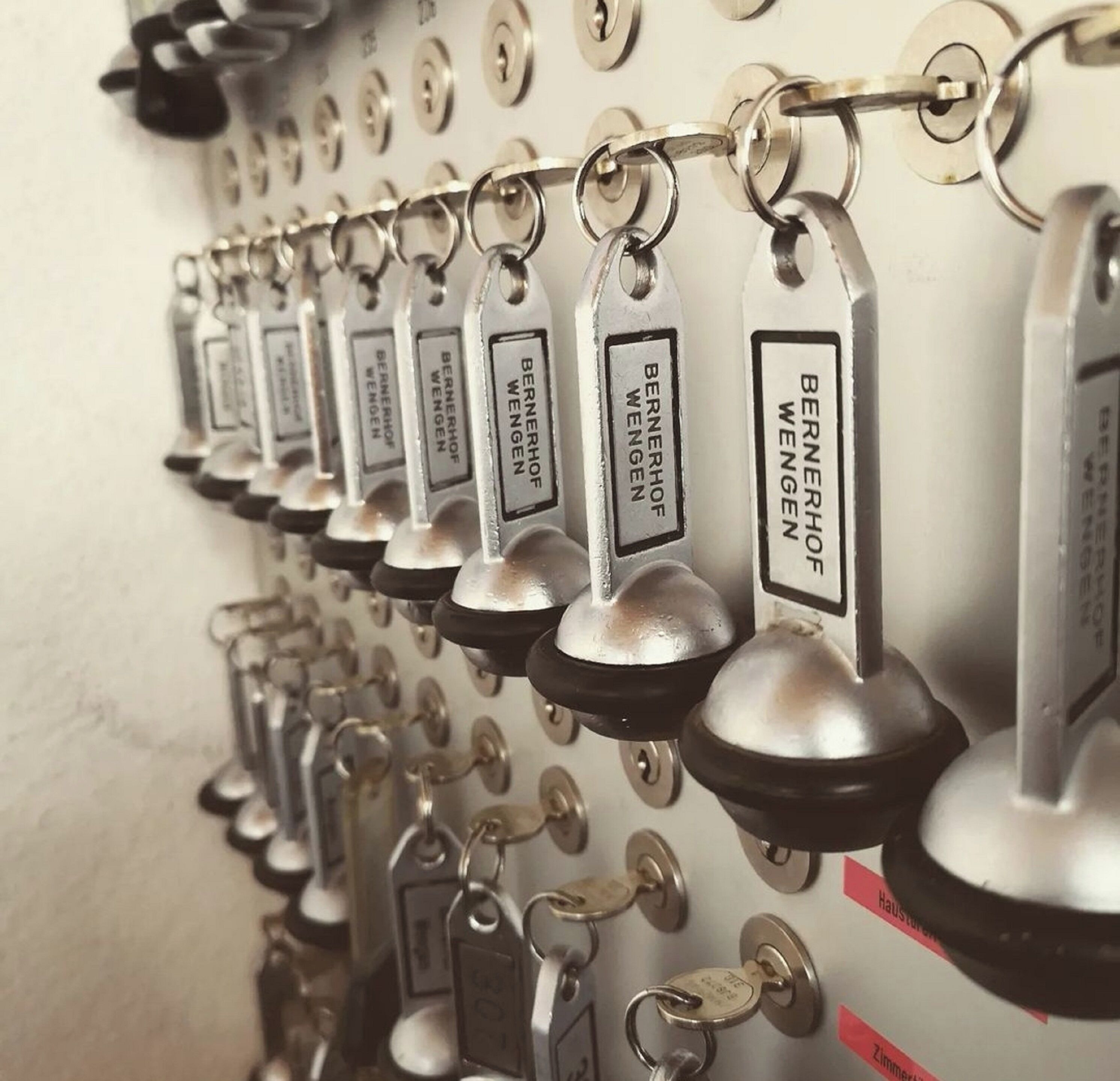 Eine Wand mit mehreren Schlüsseln, die an einer Metallvorrichtung befestigt sind, wobei jeder Schlüssel mit "BERNERHOF WENGEN" beschriftet ist.