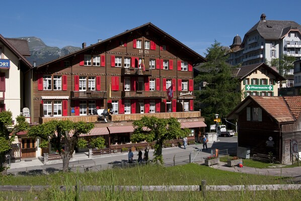 A traditional chalet-style building with a balcony, a pharmacy sign, and a mountain backdrop. - Swiss Lodge Hotel Bernerhof Wengen (Lauterbrunnen)