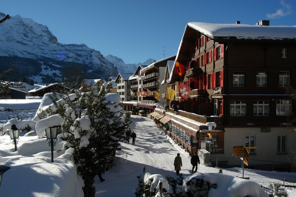 Una calle nevada con edificios, incluyendo un hotel con balcones y banderas.