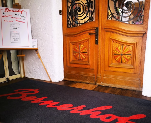 A hotel entrance with a wooden door, a welcome sign, and a doormat with the hotel's name. - Swiss Lodge Hotel Bernerhof Wengen (Lauterbrunnen)