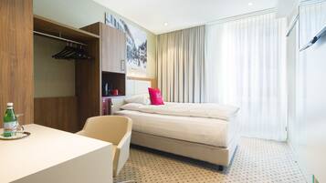A hotel room with a bed, a desk, a chair, a wardrobe, and a window with curtains.