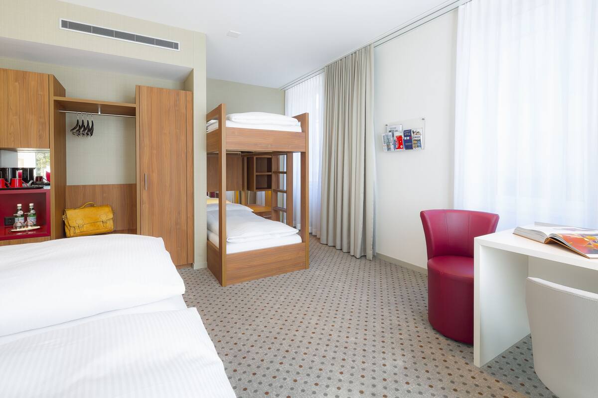 Een hotelkamer met een stapelbed, een bureau, een stoel, een kledingkast en een kleine kitchenette.