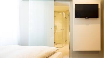 Une chambre d’hôtel avec un lit, un téléviseur fixé au mur et une cabine de douche en verre.