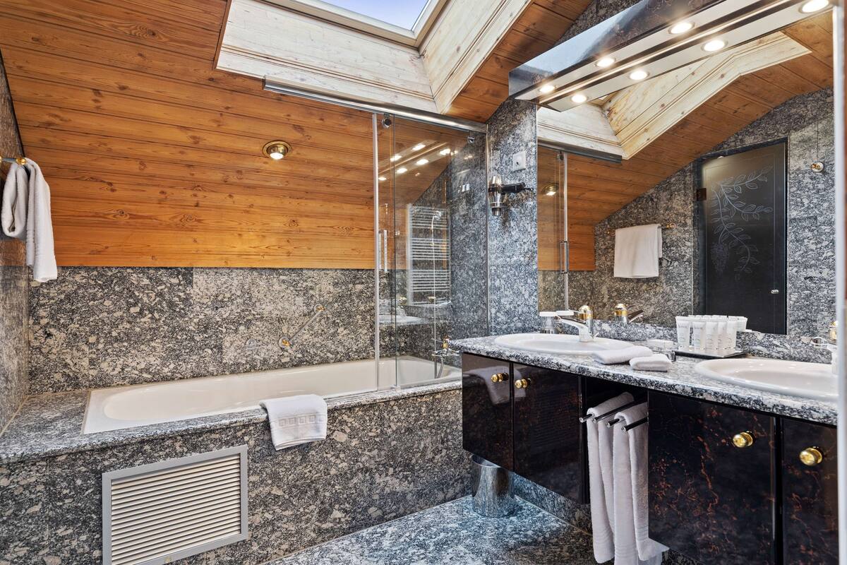 A modern bathroom with a skylight, granite countertops, a bathtub, and a large mirror.