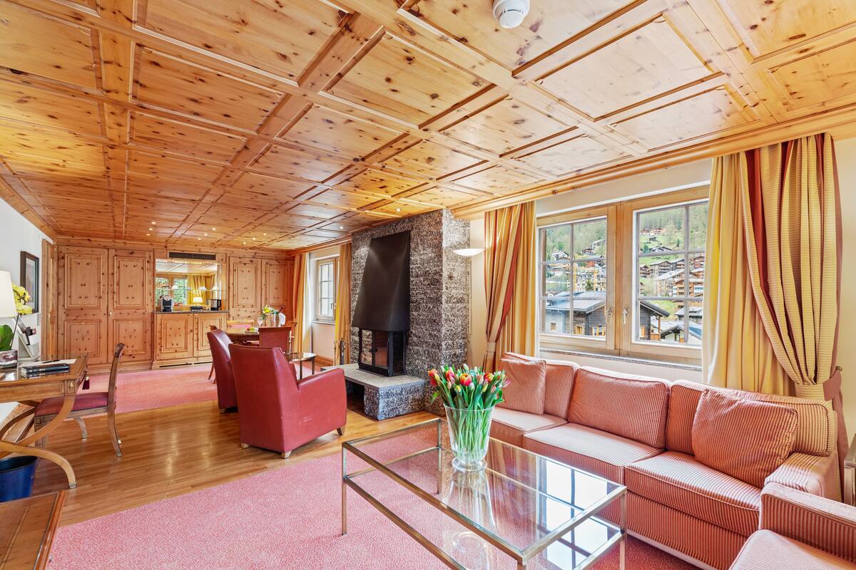 A spacious living area with a wooden ceiling, a stone fireplace, a red sofa, and a glass coffee table.