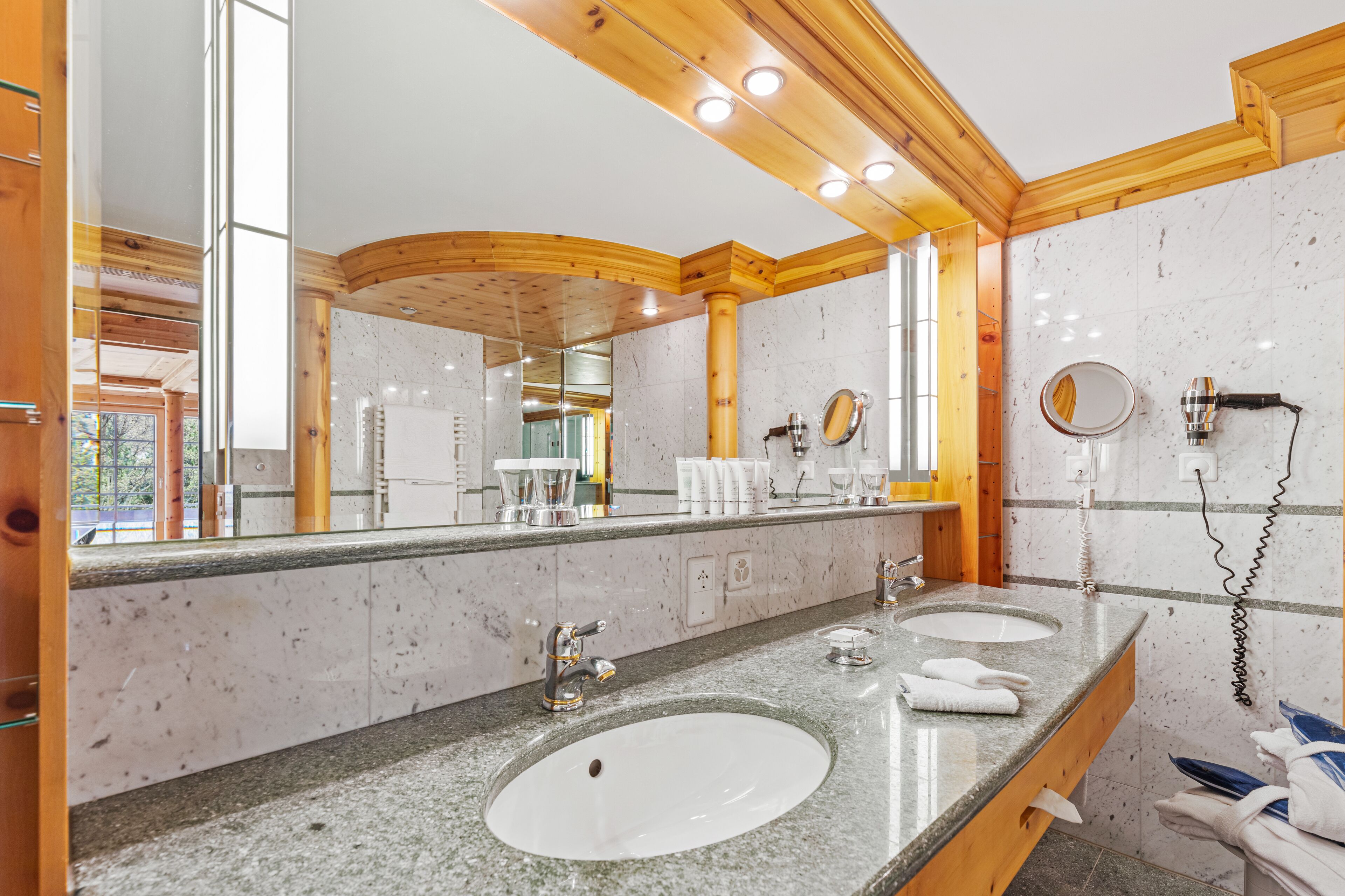 Ein modernes Badezimmer mit zwei Waschbecken, einem großen Spiegel und Holzelementen.