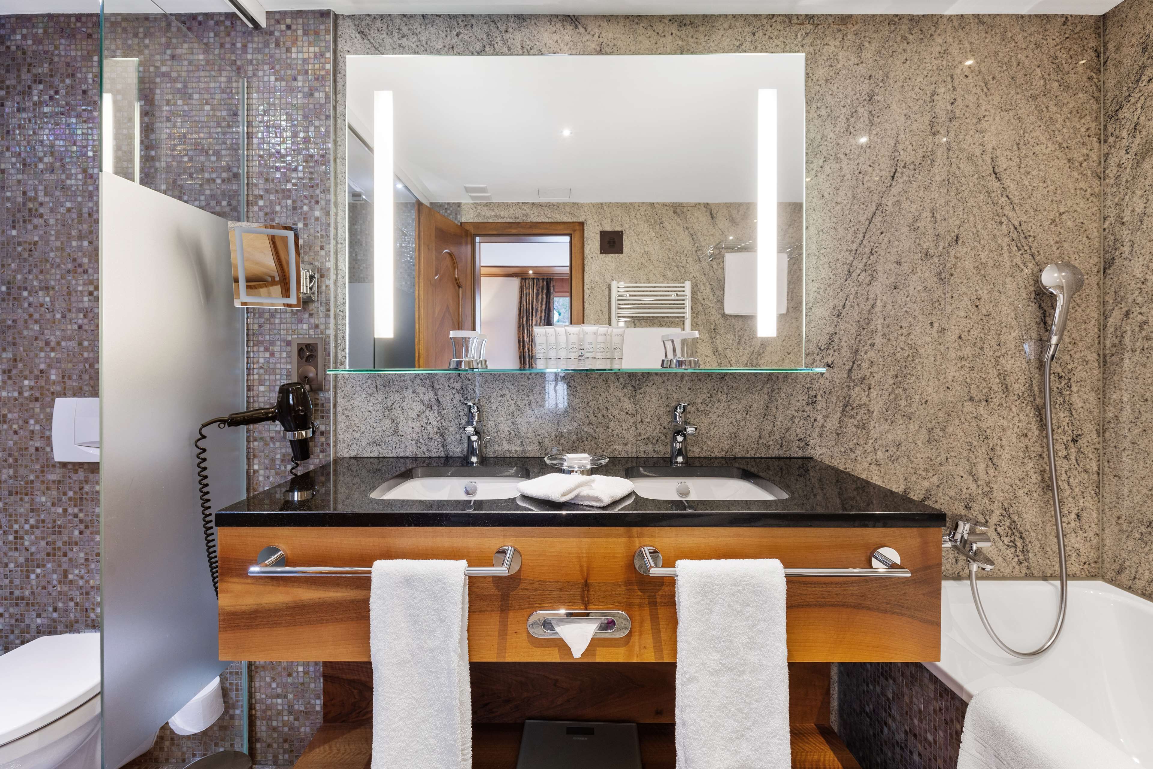 Un bagno moderno con un piano in granito, due lavabi, uno specchio grande e una doccia.