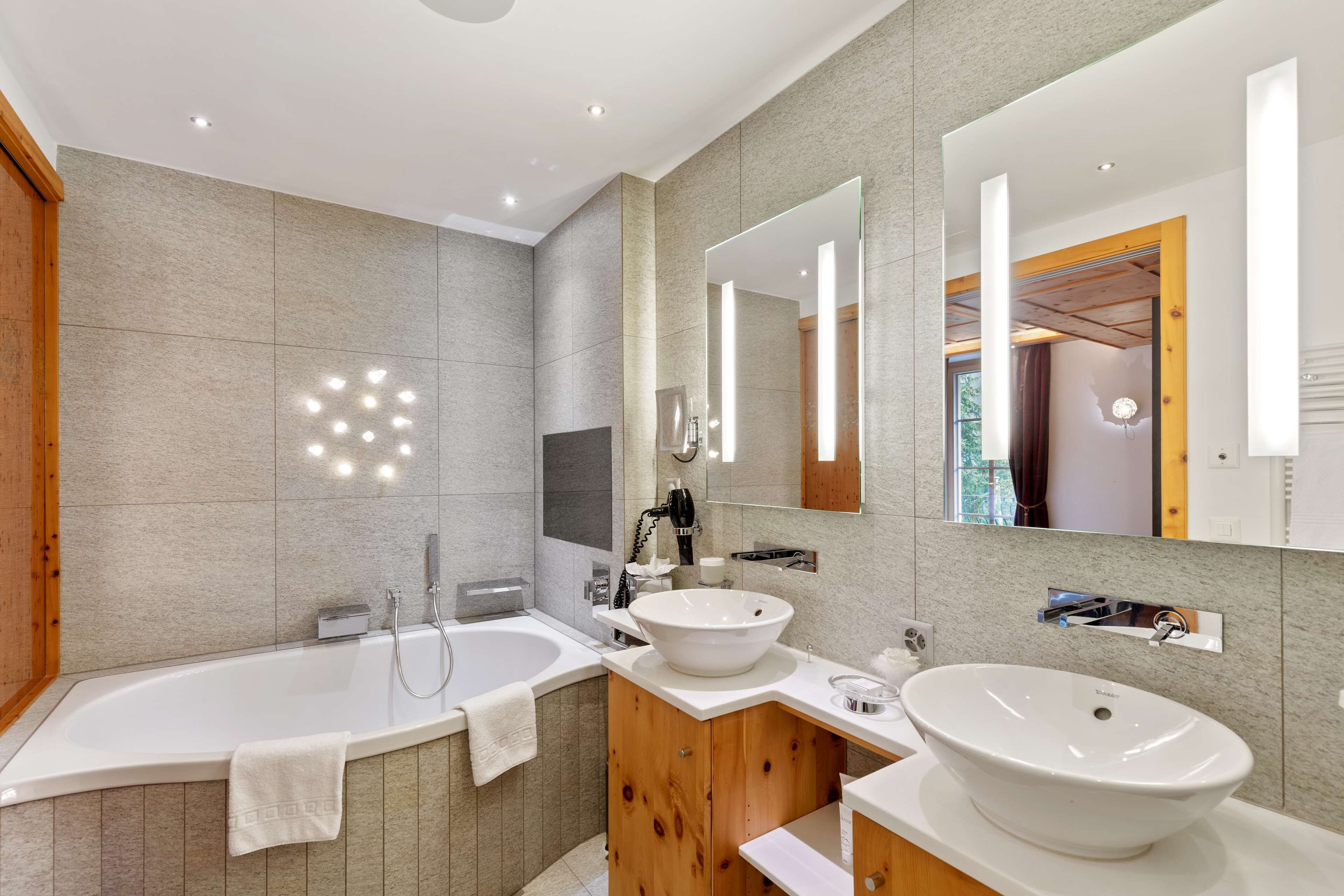 Een moderne badkamer met een vrijstaand bad, een ruim wastafelmeubel met waskom en een grote spiegel.