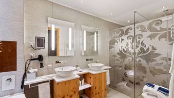 A modern bathroom with two sinks, a hairdryer, a telephone, and a glass shower enclosure.