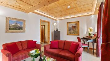 Una habitación con dos sofás a rayas rojas, techo de madera, un escritorio con silla, y dos cuadros enmarcados en las paredes.