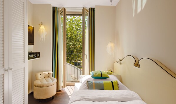 A bedroom with a bed, a chair, a nightstand, and a window with curtains. - Giardino Lago (Minusio)