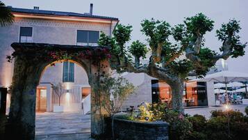 An outdoor area with a stone archway, a tree, and a building with a large window and a door.