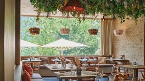 Restaurante com mesas ao ar livre, preparadas com taças de vinho e talheres, e plantas penduradas acima.