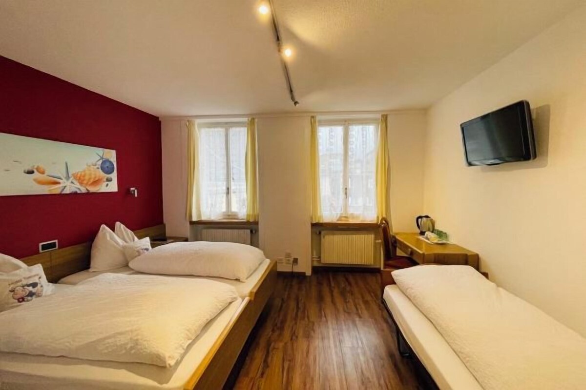 A hotel room with two beds, a television, a painting on the wall, and a window with curtains.