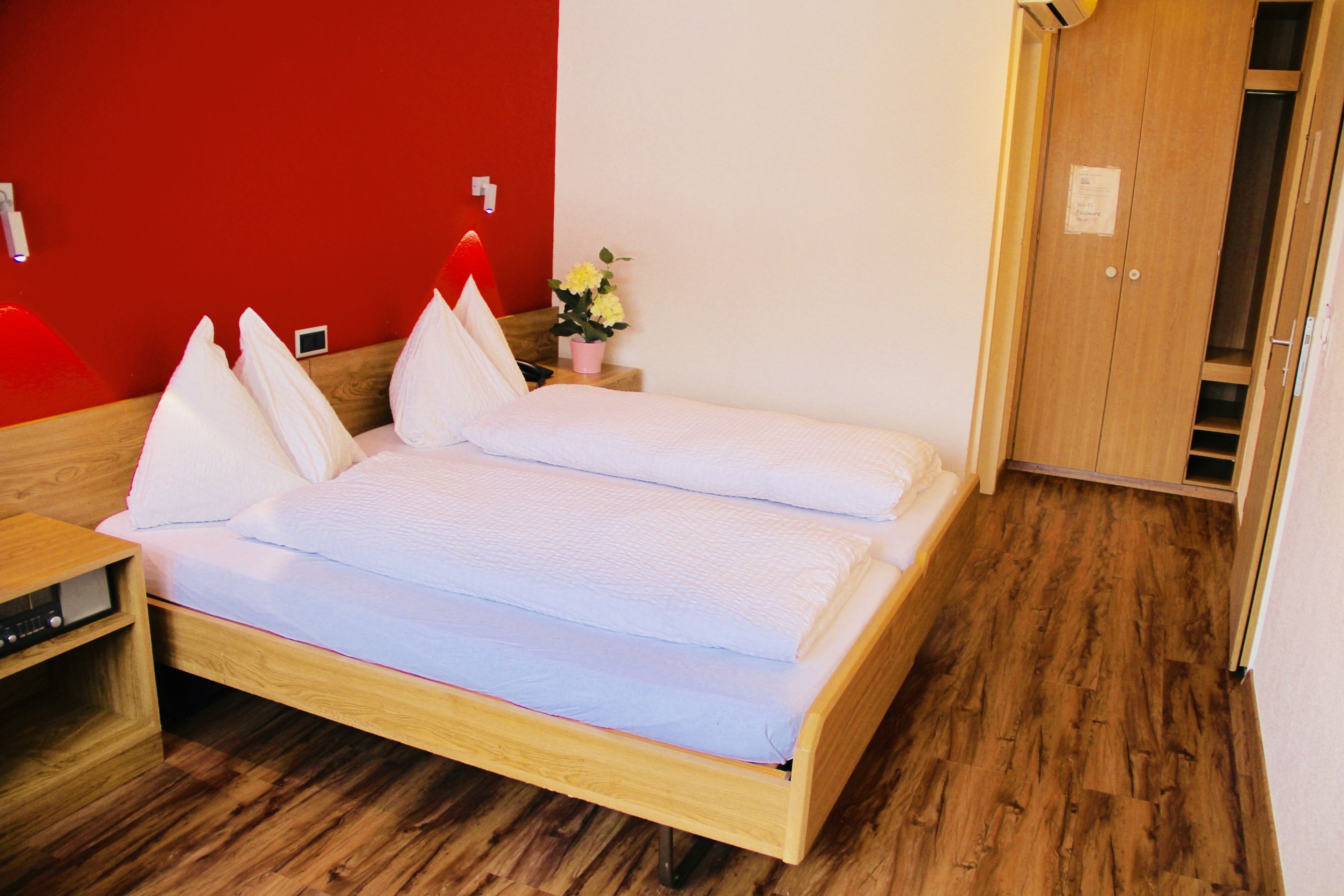 Un dormitorio con una cama de madera, una mesita de noche, una pared roja y un armario de madera.