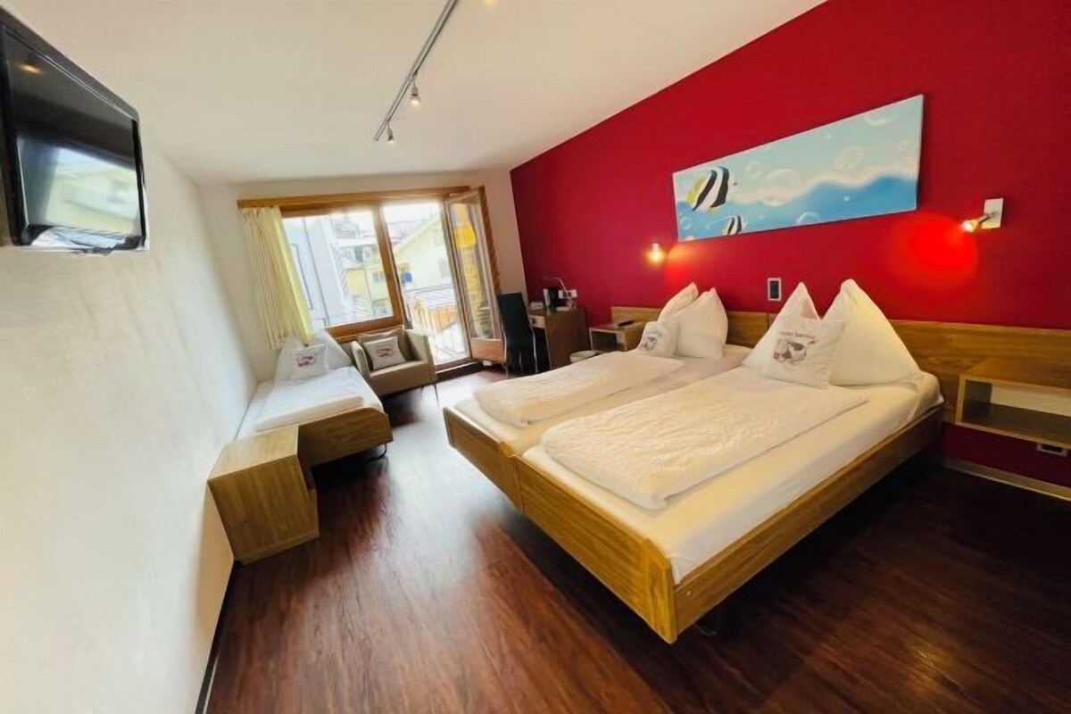 A hotel room with a wooden bed, a desk, a chair, a TV, and a large window with curtains.