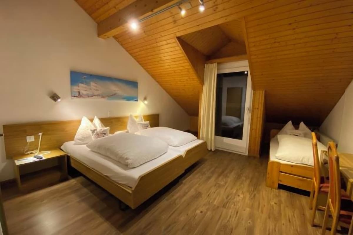 A bedroom with a wooden ceiling, a bed, a nightstand, a chair, and a window.