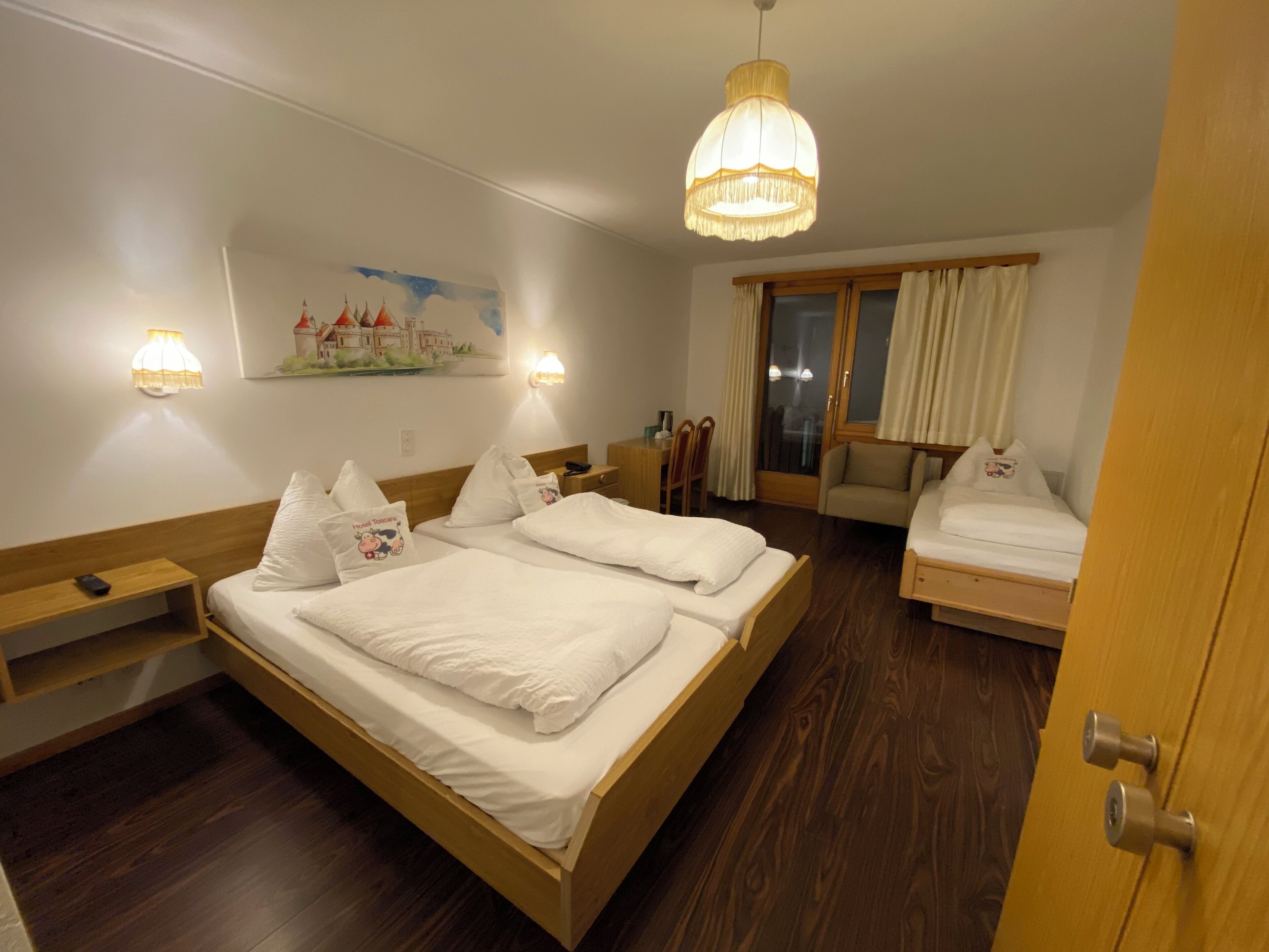 Een hotelkamer met twee bedden, een bureau, een stoel en een groot raam met gordijnen.