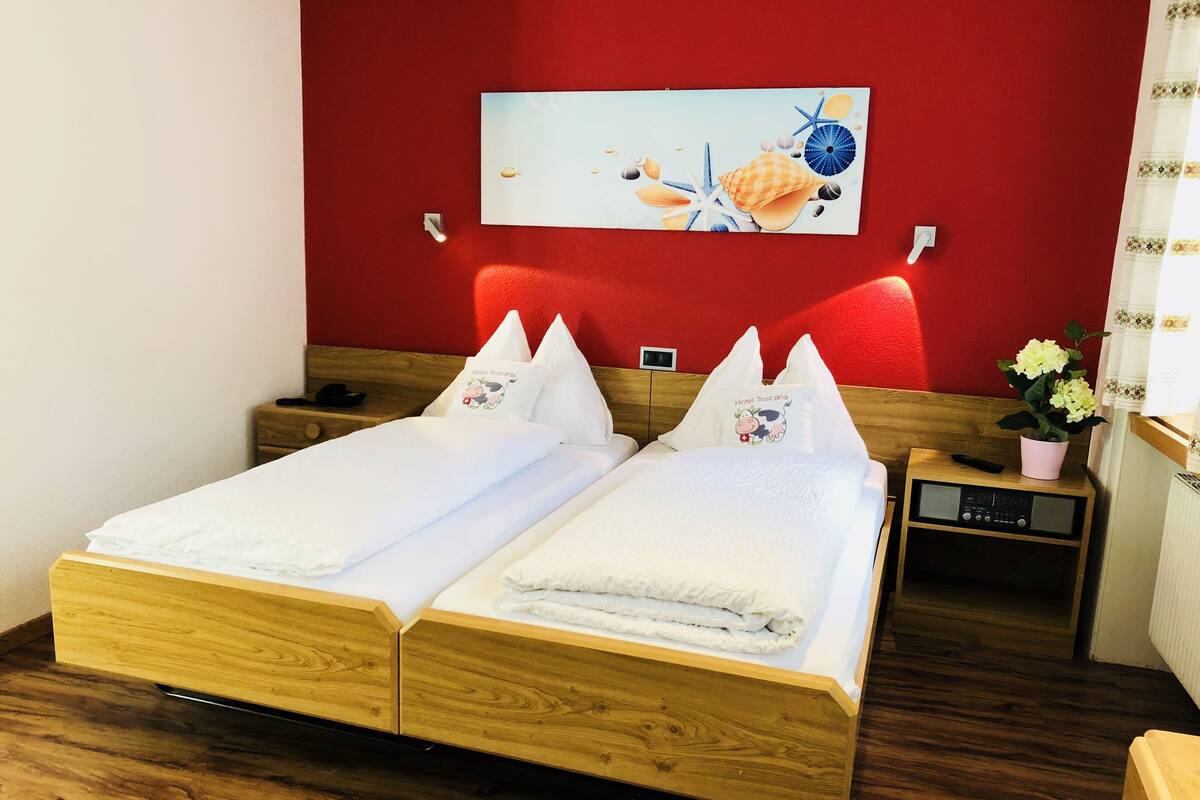 A double bed with white linens, a wooden headboard, and a red accent wall.