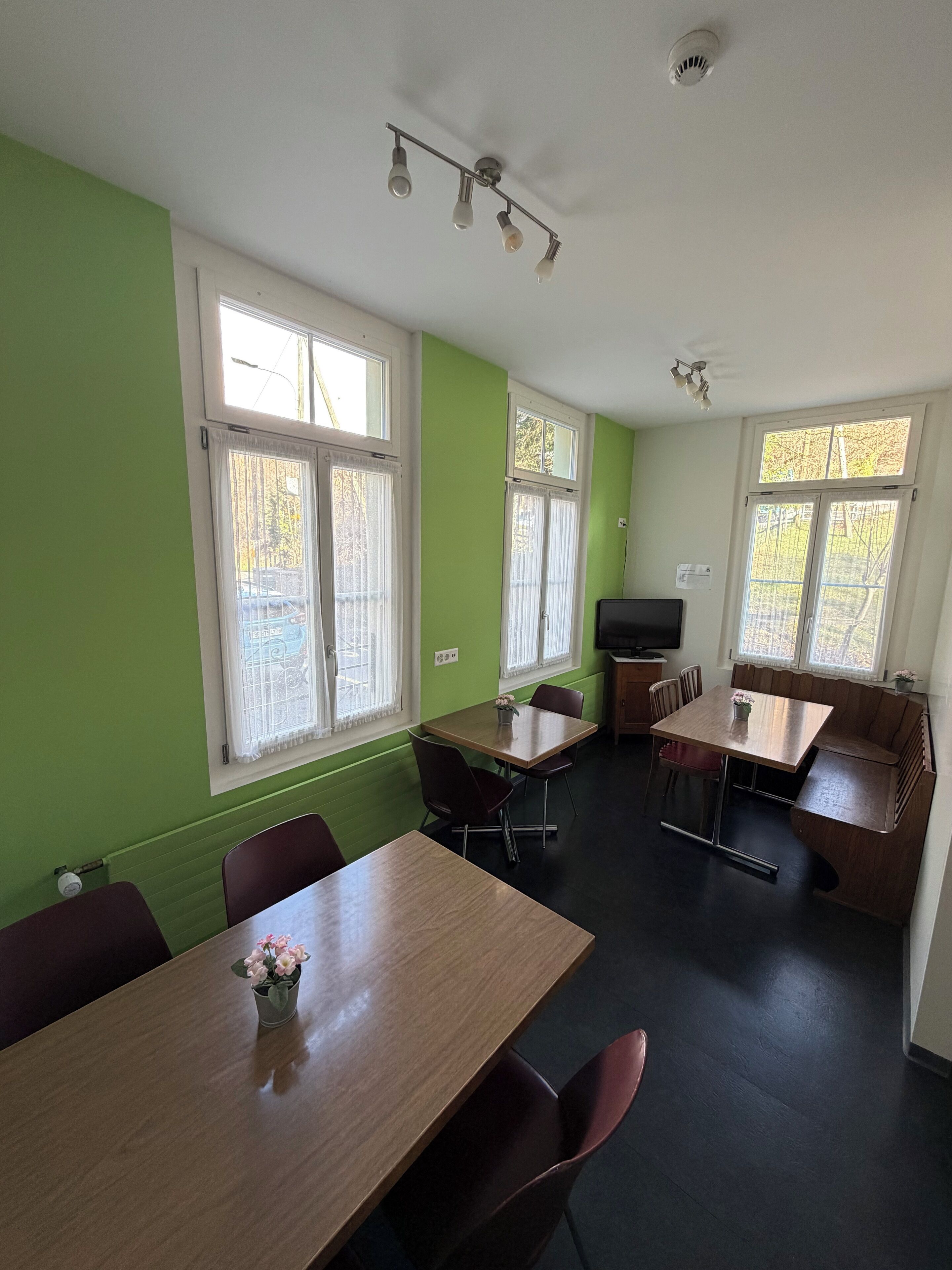 A room with a green wall, a wooden table with chairs, a bench, and a television.