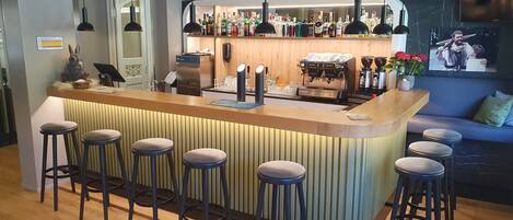 Una zona de bar con taburetes, una máquina de café y una variedad de botellas.