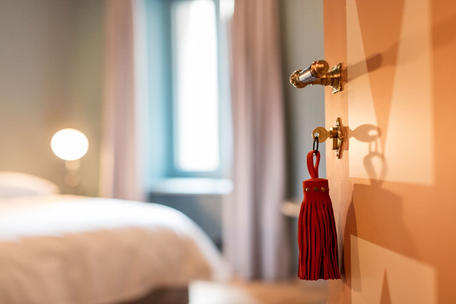 Une chambre d’hôtel avec un lit, une porte dotée d’une poignée en laiton et une frange rouge qui pend à la porte.