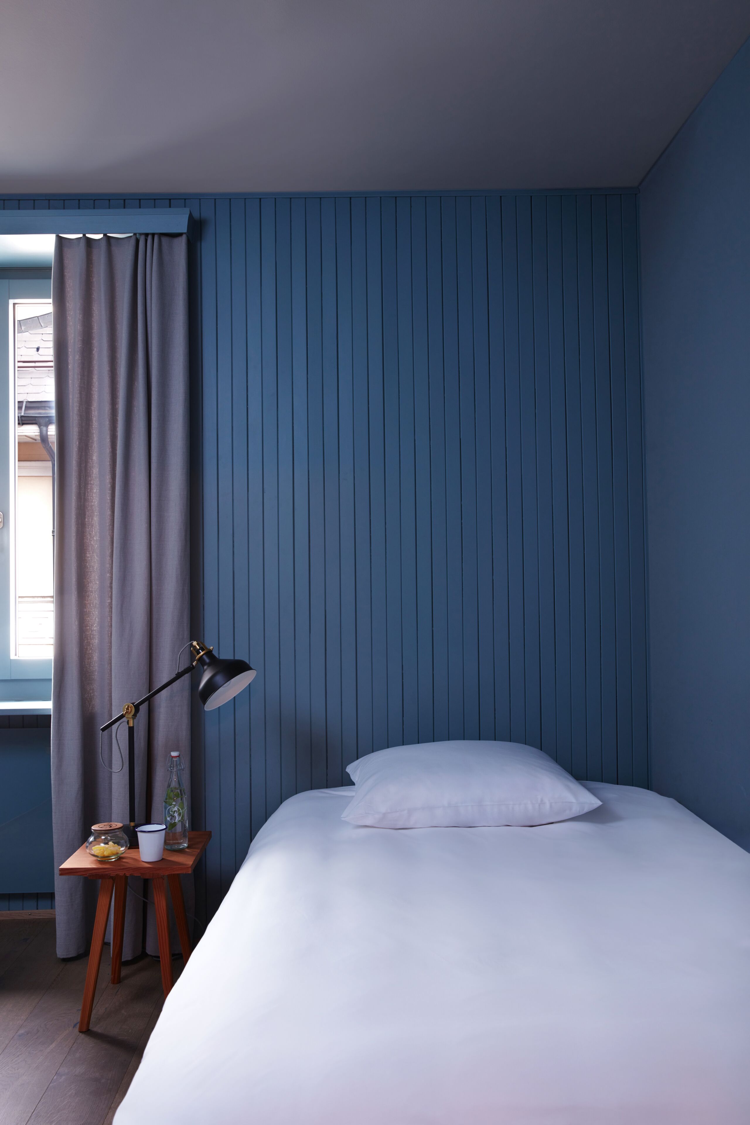 A bedroom with a bed, a nightstand, a lamp, and a window with curtains.