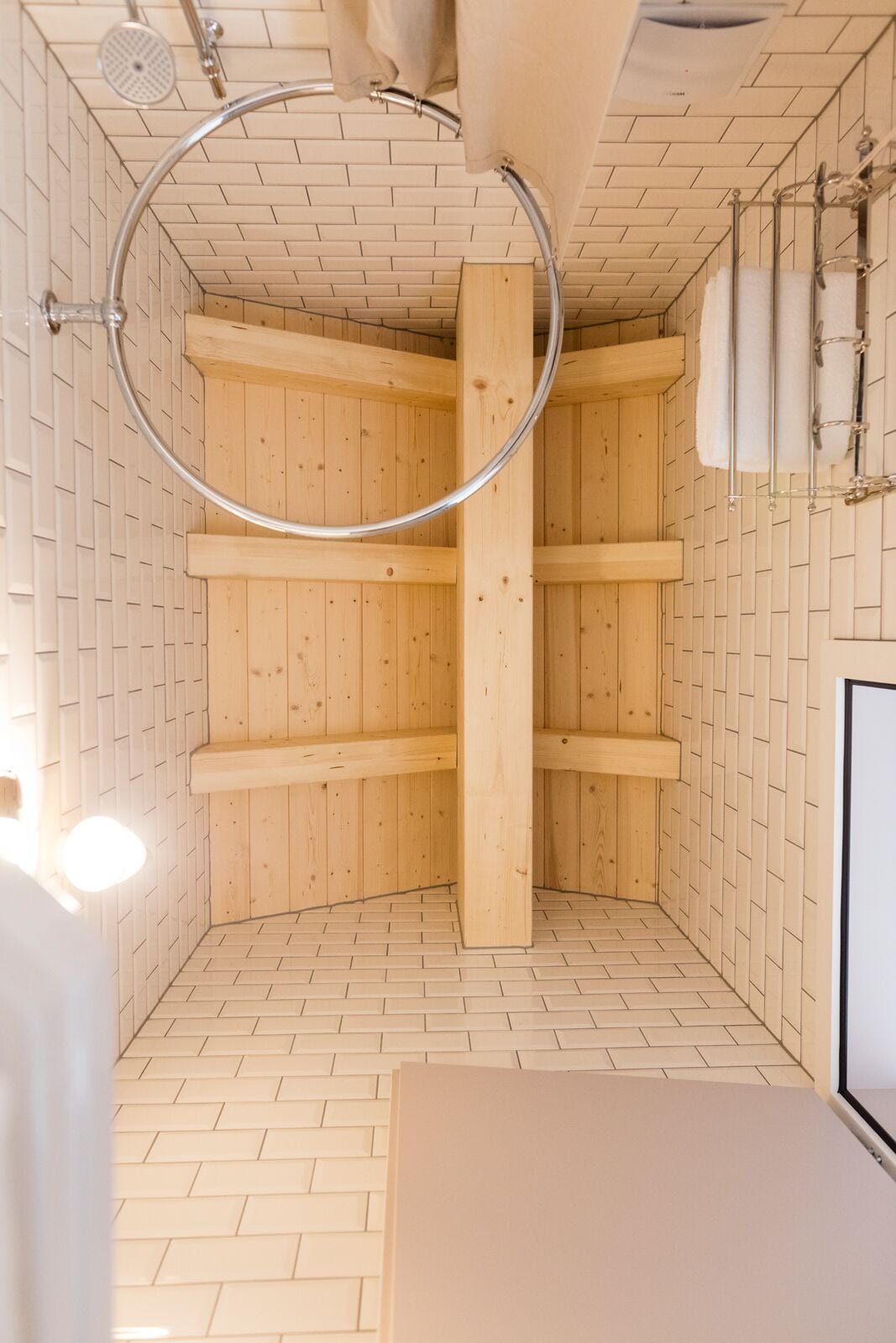 Un sauna aux murs en bois et au sol carrelé, comprenant un espace de douche circulaire et des porte-serviettes.