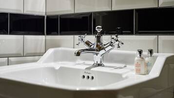 Casa de banho com lavatório branco, torneira cromada e duas embalagens de sabonete líquido na bancada.