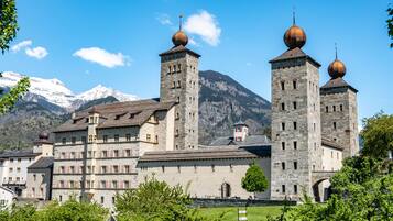 Un bâtiment historique doté de nombreuses tours et d’une cour centrale, entouré de montagnes aux sommets enneigés.