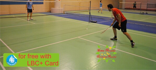 An indoor badminton court with players and a net. - Paradis (Leukerbad)