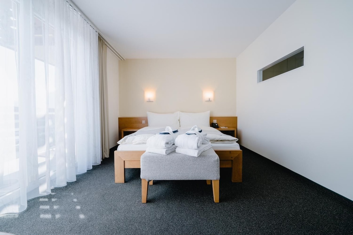 Quarto de hotel com cama, mesas de cabeceira, janela com cortinas e piso coberto por carpete.