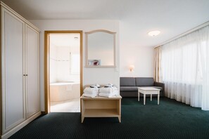 Quarto de hotel com uma cama, um sofá, uma mesinha, um espelho e uma janela com cortinas.