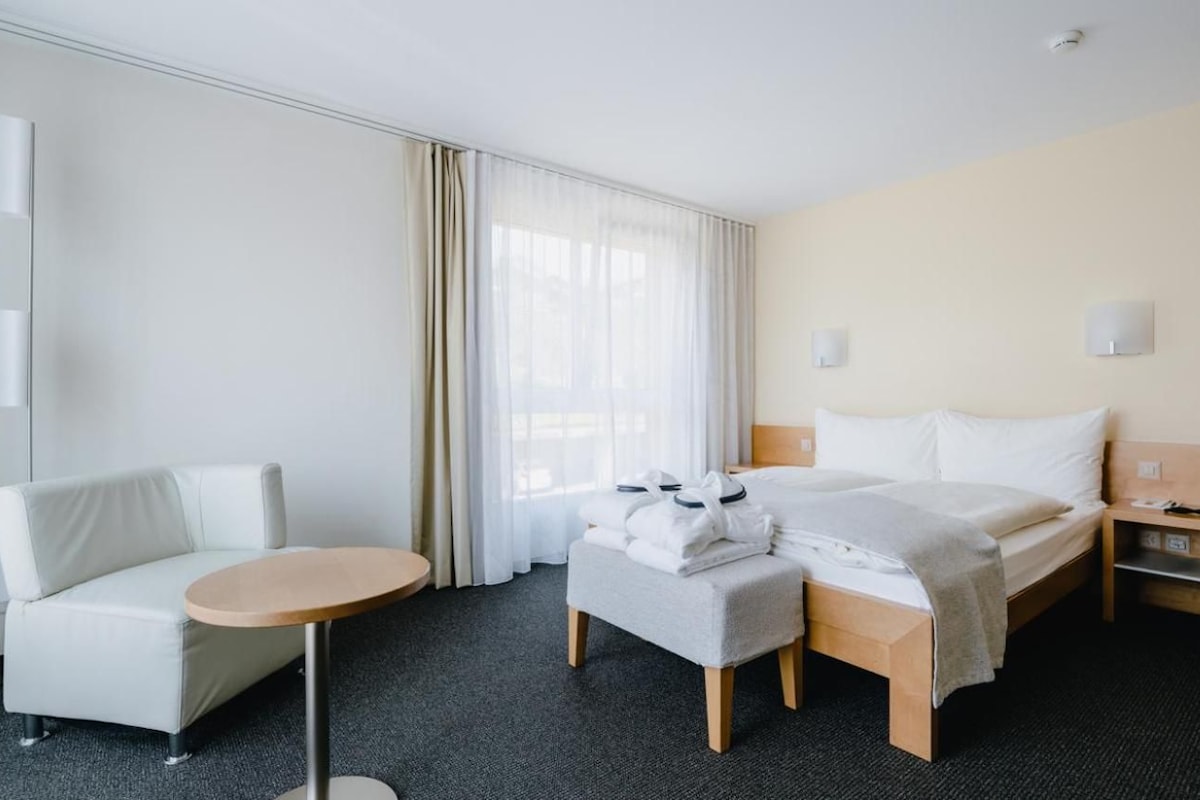 Quarto de hotel com uma cama, um sofá, uma mesinha e uma mesa de cabeceira.