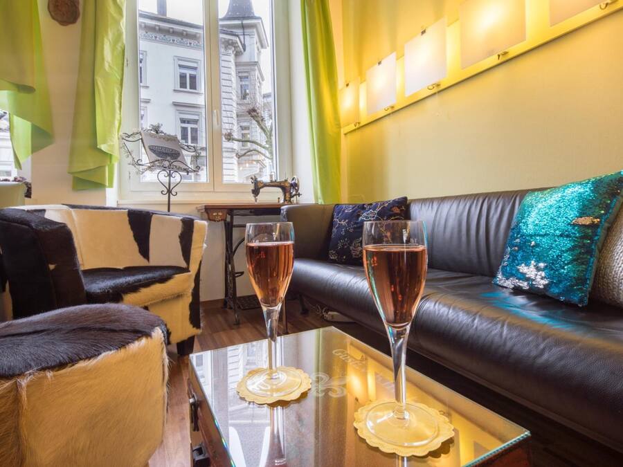 Ein gemütliches Wohnzimmer mit einem Ledersofa, zwei Sesseln und einem Glastisch mit zwei Sektgläsern.