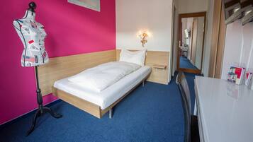 A hotel room with a bed, a mannequin, a nightstand, a mirror, and a desk.