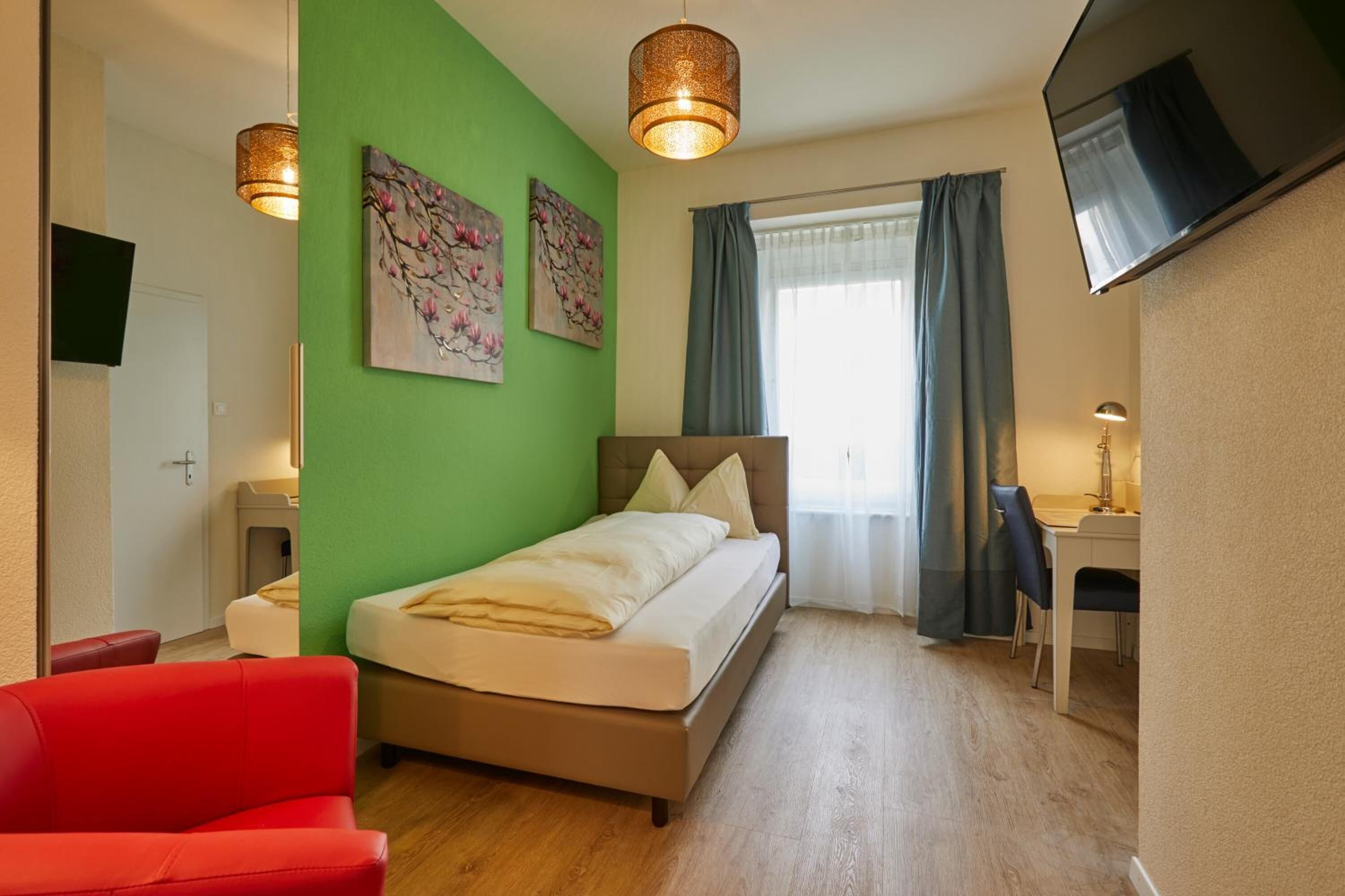 Una camera da letto con un letto, una scrivania, una sedia, un divano rosso e opere d'arte alle pareti.