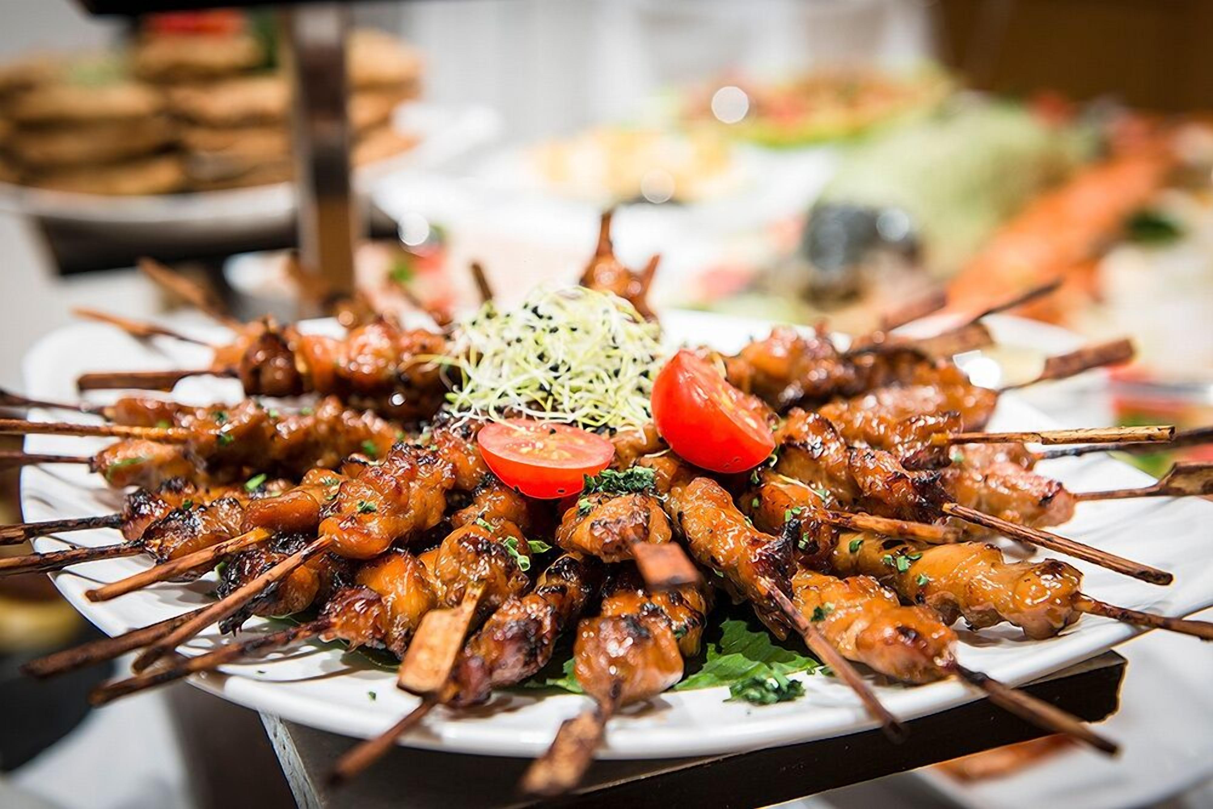 Un plato de brochetas de carne adornado con repollo rallado y rodajas de tomate.