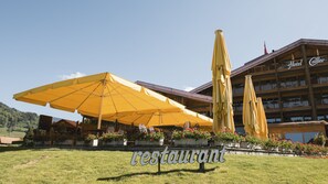 A hotel with outdoor seating under yellow umbrellas, a sign reading "restaurant," and a building with balconies. - Hotel Cailler (Charmey)
