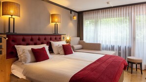 Ein Hotelzimmer mit einem großen Bett, zwei Nachttischen, einem roten, gepolsterten Kopfteil und einem Fenster mit durchsichtigen Vorhängen.