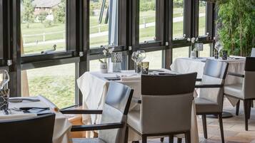 Un restaurante con mesas dispuestas para comer, ventanas amplias que ofrecen vistas al exterior y un interior ordenado.