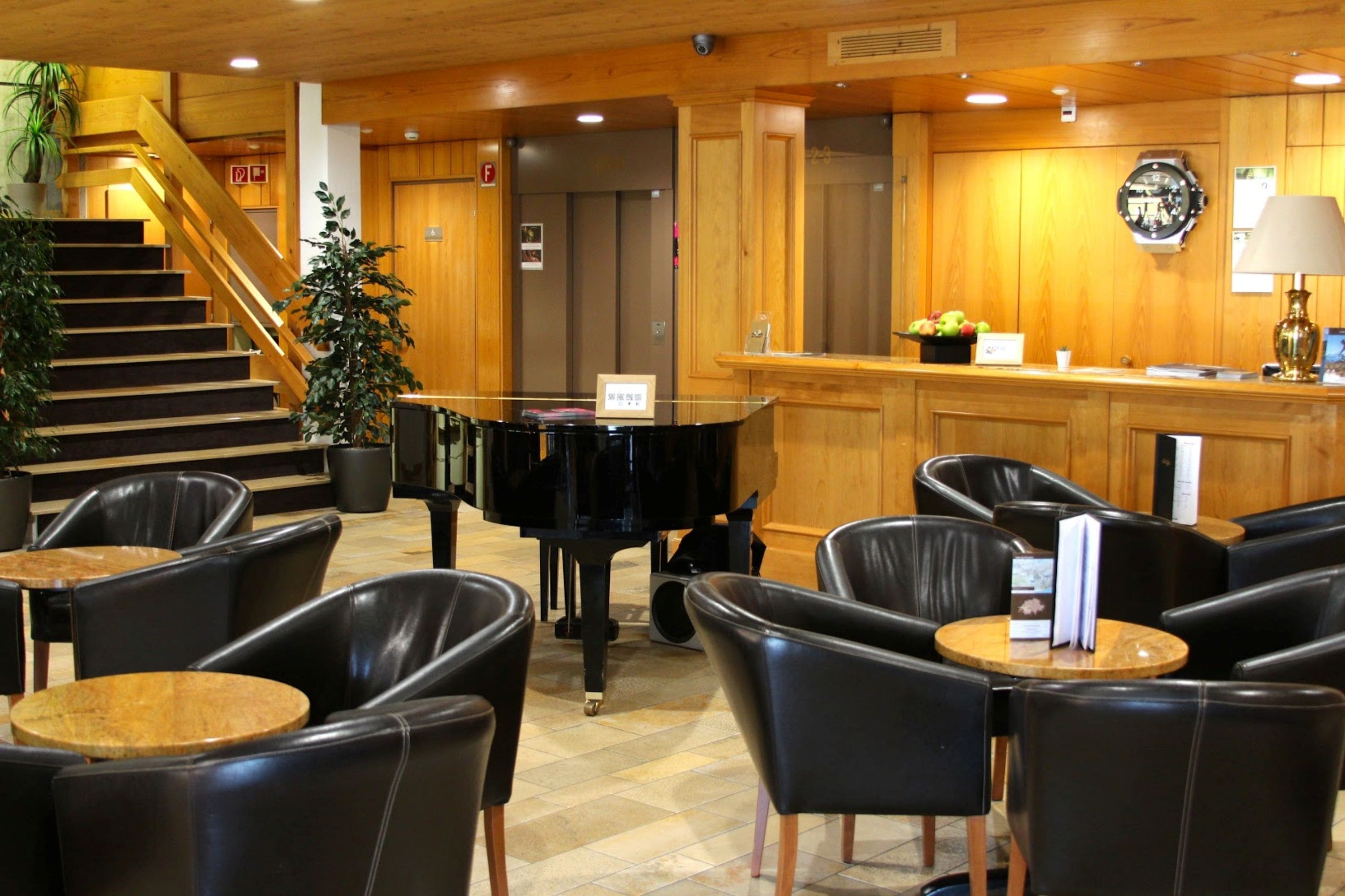 A lobby with a grand piano, leather chairs, a staircase, and wooden paneling.
