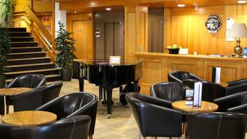 A lobby with a grand piano, leather chairs, a staircase, and wooden paneling.